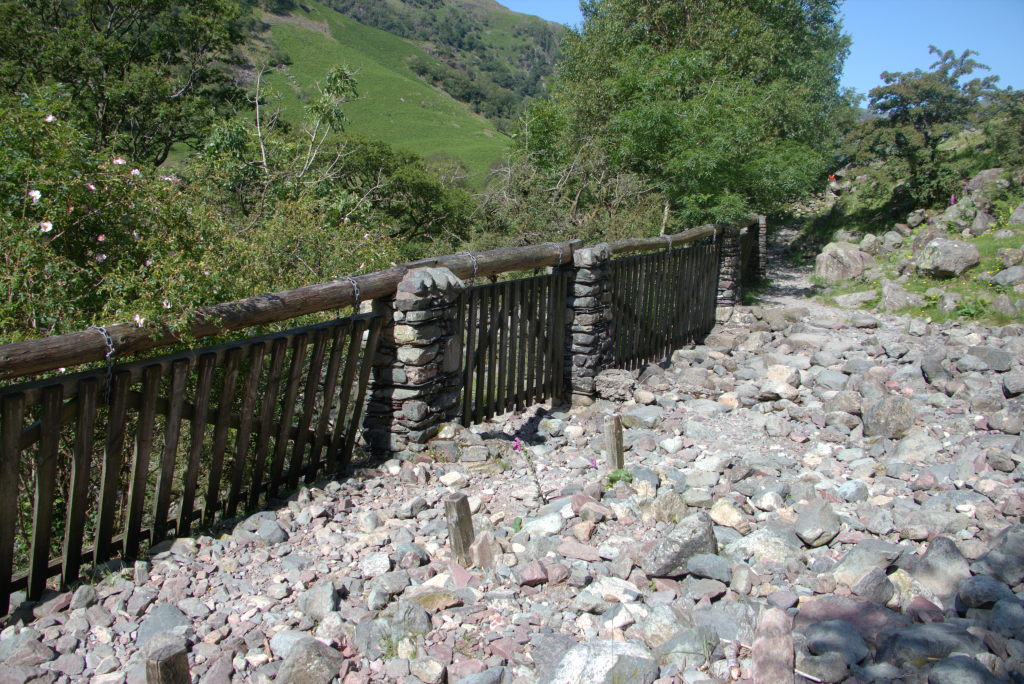 Der Pfad durchquert ein Geröllfeld mit einem Zaun aus hängenden Gattern, die aus dem Weg schwingen können, wenn Wasser den Berg runterrauscht