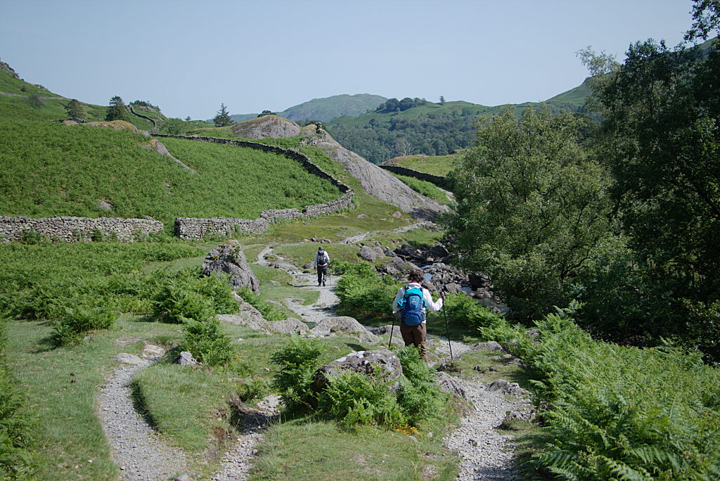 Manu von hinten bei der Wanderung durch ein Tal. Im Hintergrund läuft ein Mann voraus.