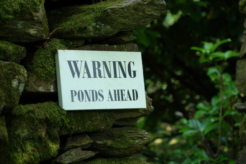 A sign on a drystone wall reading "Warning, Ponds ahead"