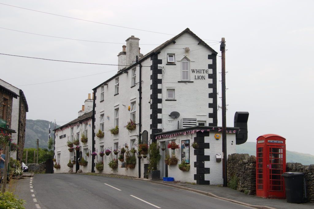 Das White Lion Inn in Patterdale von der Straße aus. Ein schmales weißes Haus mit schwarzen Akzenten an den Ecken