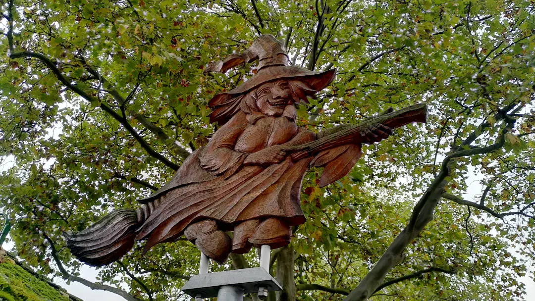 Eine aus Holz geschnitzte Hexe auf dem Besen, die den Start des Hexenstiegs markiert