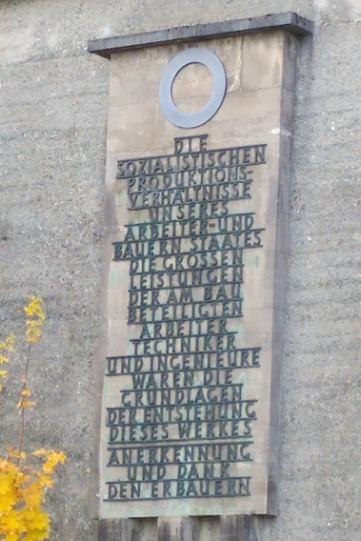 A large concrete plaque with the inscription: "The socialist production conditions of our workers' and peasants' state, the great achievements of the workers, technicians, and engineers involved in the construction, were the foundations of the creation of this work. Recognition and thanks to the builders." (Spelling and punctuation are weird in the original)