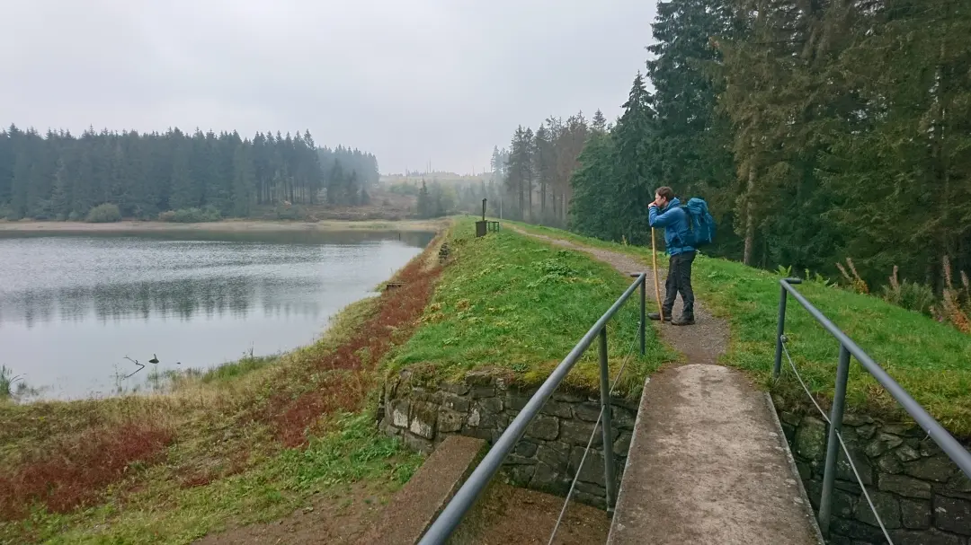 Markus rests his chin on his hiking stick and looks out over a half-empty reservoir