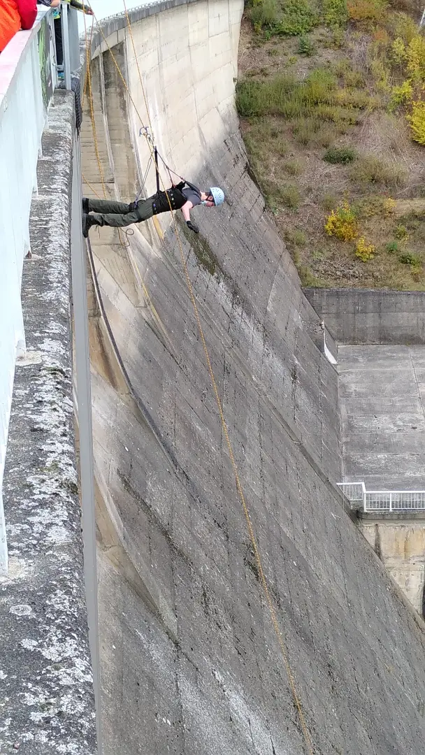 A man, secured by a rope, hangs face down on the outside of a dam