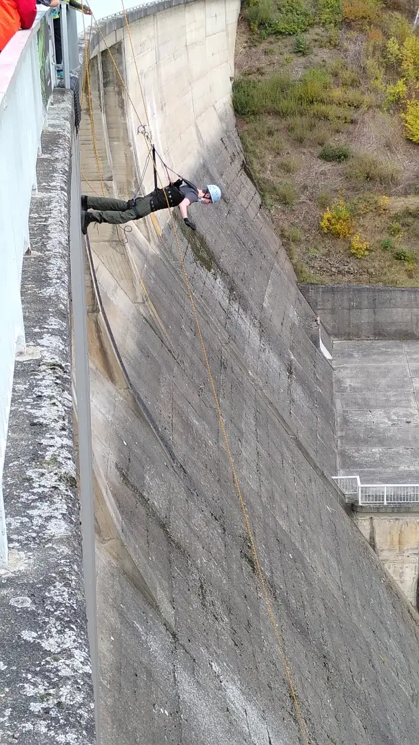 Ein Mann steht, am Seil gesichert, mit dem Gesicht nach unten an der Außenseite einer Staumauer