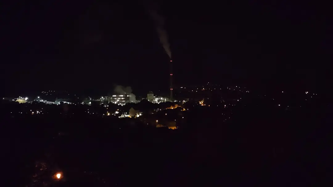 Blick über Alfeld bei Nacht. Man sieht vereinzelt Lichter und die roten Warnlampen des großen Industrieschornsteins in der Bildmitte