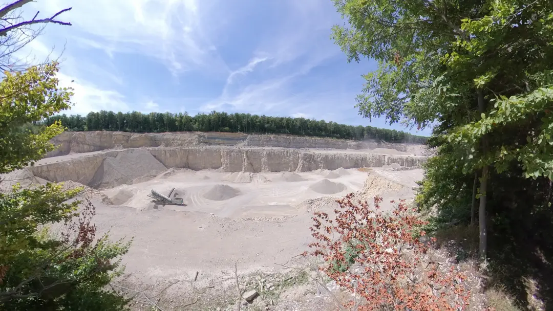 Blick über einen großen Kalksteinbruch, dessen weißer Kalkstein sich gut vom grünen Hintergrund des Waldes abhebt