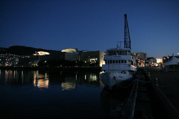 Ein Blick über den Hafen im Dunkeln. Im Vordergrund ein altes Schiff, im Hintergrund Te Papa