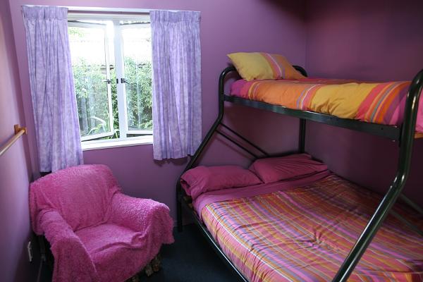 Blick in ein Hostelzimmer mit einem Doppelstockbett. Alles ist in pink und lila gehalten, inklusive Wände und Sessel