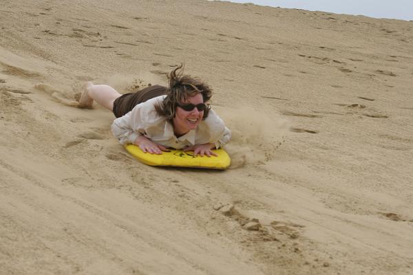 Manu auf einem Sandboard eine Düne runterrutschend