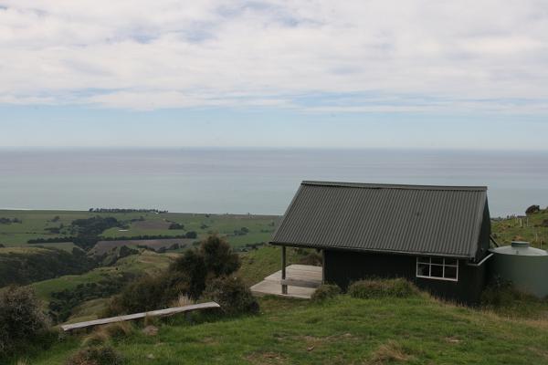 Blick auf eine Hütte am Berg mit Ozean im Hintergrund