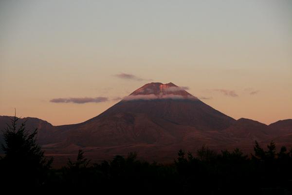 Bild des Vulkans im Licht der untergehenden Sonne. Um den Gipfel treiben ein paar dünne Wolken.