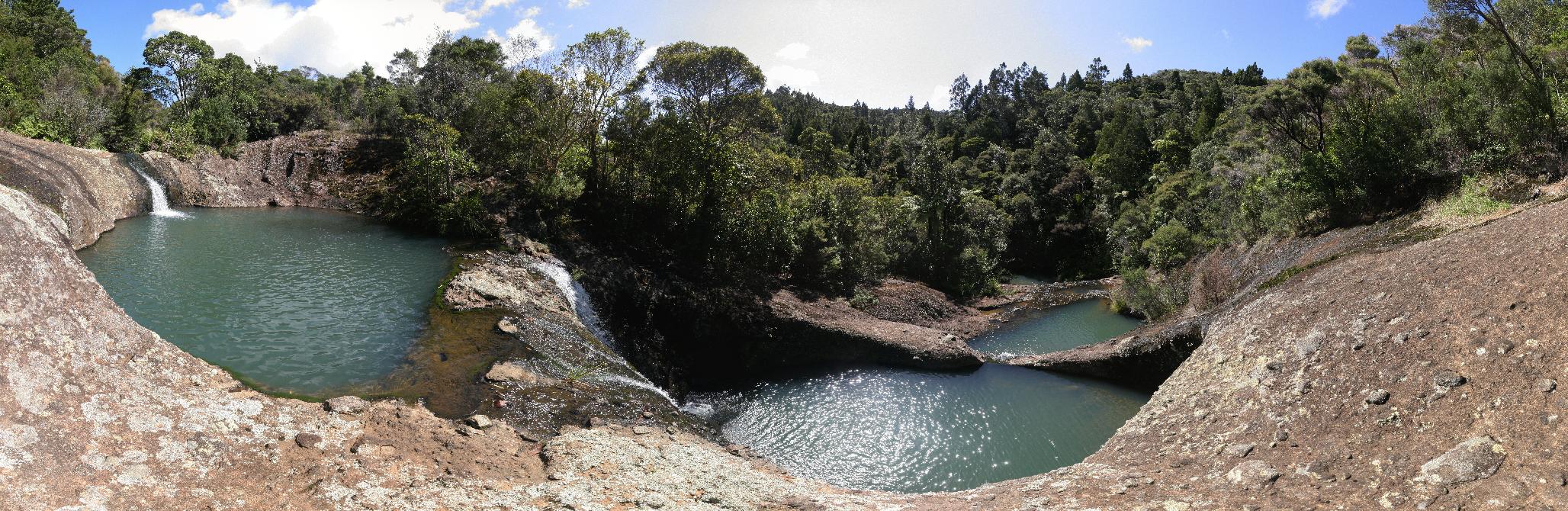 Ein Panorama von drei stufenförmig angeordneten, natürlichen Pools, die ein Bach in eine Felsplatte geschnitten hat