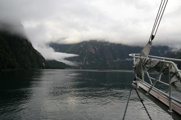 Blick über den Bug eines Schiffes ins wolkenverhangene Fjord