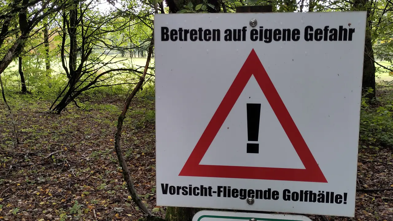 A sign reading "Enter at your own risk. Beware – flying golf balls!"