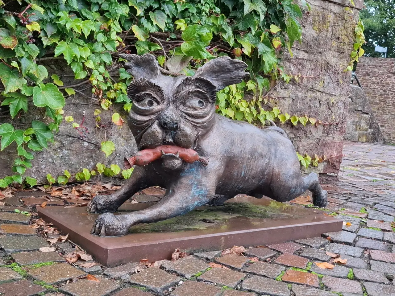 A bronze statue of a small dog running away with a sausage in its mouth