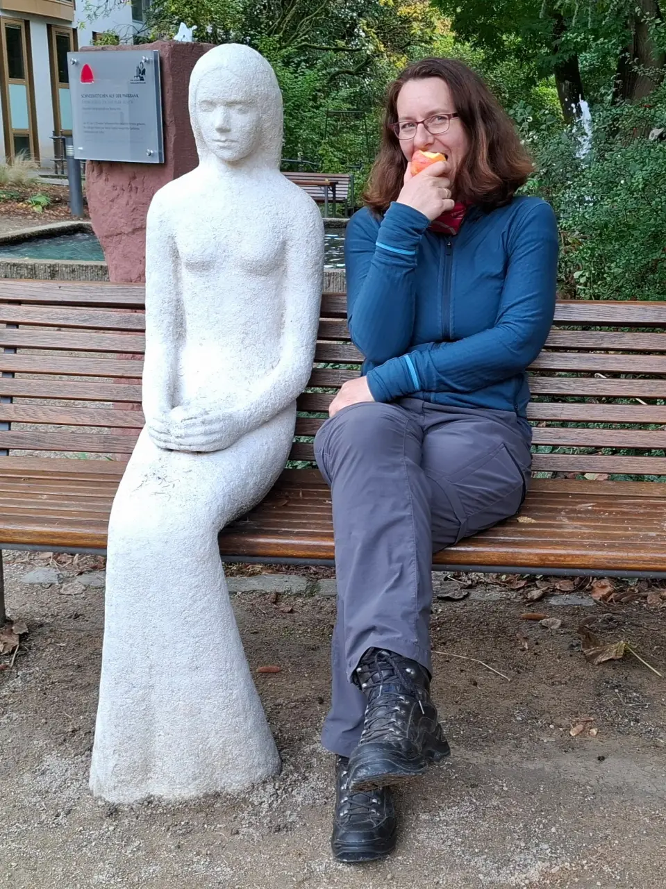 Manu sitting next to a stone statue of Snow White on a bench while happily biting into an apple